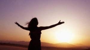 Serene-young-woman-with-arms-outstretched-doing-yoga-in-the-desert-in-Silhouette